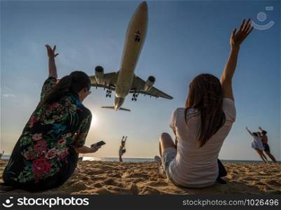 Scene of Two traveler woman showing hand and funning with Airplane landing closely at the sea beach beside the phuket international airport, Thailand