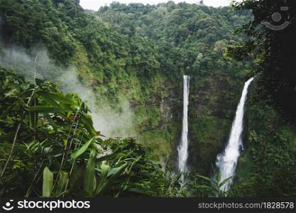Scenery of Tad Fane waterfall in the morning mist. Great twin waterfalls in rainy season. Green tropical forest covers ravine and mountains in the backgrounds. Bolaven plateau, Laos.