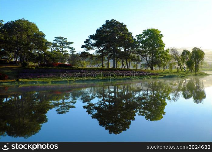 Scenery of Than Tho lake, Da Lat city, Viet Nam in morning, pine tree in forest reflect on water make romantic and fresh view for ecotourism in summer