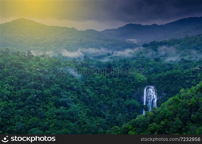 Scenery of tropical waterfall in the morning mist, stunning aerial view of waterfall in a tropical rainforest at sunrise. Khlong Lan National Park, Thailand. Long exposure. Soft focus on waterfall.