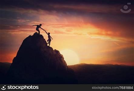 Scenery view with a team of two climbers on the top on the mountain. Person helping another to overcome obstacles and reach the top together. Teamwork concept, working in group to achieve success