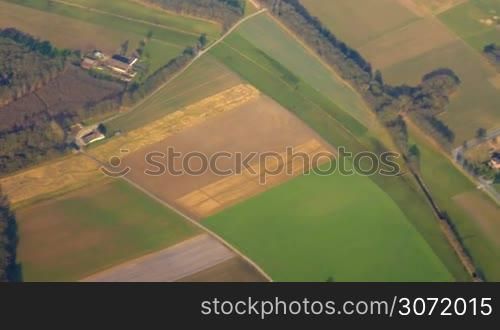 Scenic aerial view to the small town with vast green fields around. Enjoying beautiful nature scenes from the flying airplane