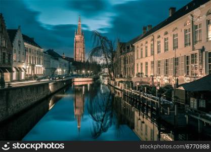 Scenic cityscape with a medieval fairytale canal and the quay Dijver and Church of Our Lady at sunset in Bruges, Belgium. Toning in cool tones