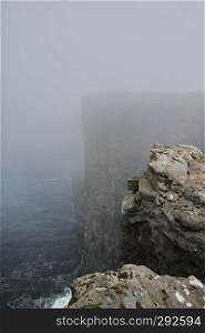 Scenic image to cliffs and North Atlantic Ocean covered by fog near the lake Sorvagsvatn or Leitisvatn Lake on Island Vagar of the Faroe Islands. Glorious sceneries of the Faroes. Postcard motif.
