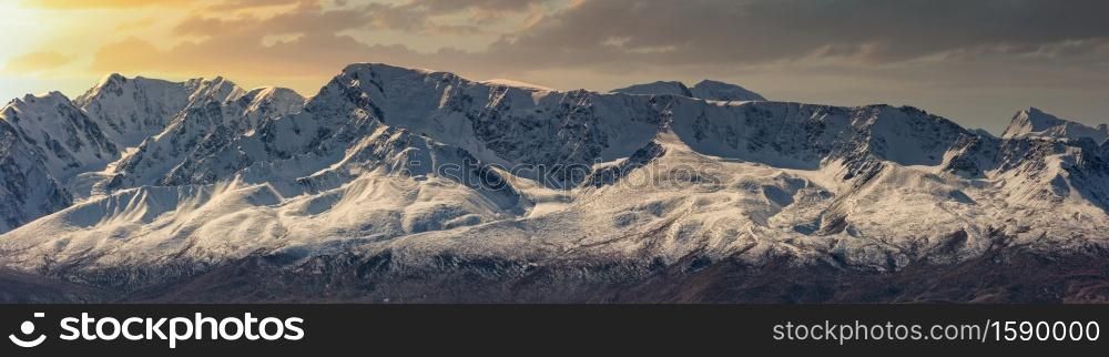 Scenic panoramic aerial view of snowy mountain peaks and slopes of North Chuyskiy ridge at sunset. Beautiful cloudy orange sky as a background. Altai mountains, Siberia, Russia.. Scenic panoramic aerial view of snowy mountain peaks and slopes of North Chuyskiy ridge at sunset. Beautiful cloudy orange sky as a background. Altai mountains, Siberia, Russia