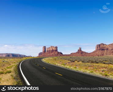 Scenic road in desert landscape with mesa and mountains.