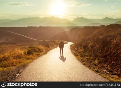 Scenic road in the mountains. Travel background. Man going on sunrise background.