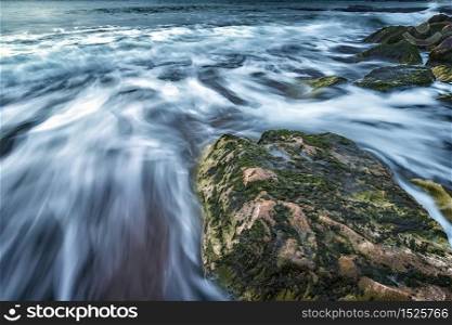 Scenic seascape of a big rock and waves flowing out