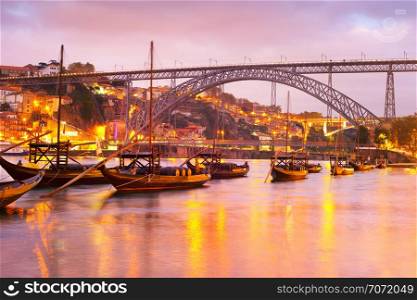 Scenic sunset over Douro river with traditional wine boats, illuminated Porto skyline and Dom Luis I bridge in background, Portugal