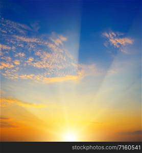 Scenic sunset with sun rays against bright blue sky and clouds