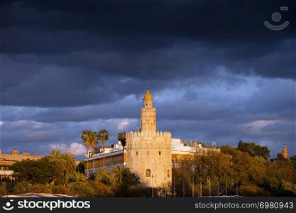 Scenic Torre del Oro (Gold Tower) at sunset with storm clouds above, medieval landmark from early 13th century in Seville, Spain, Andalusia region.