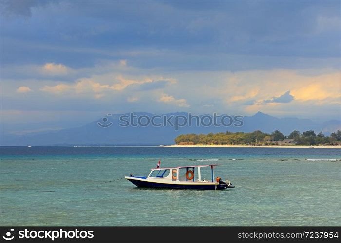 Scenic tropical Indonesian island with anchored boat against a dark sky with clouds