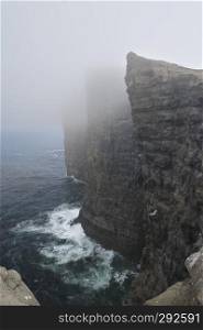 Scenic vertical image to cliffs and North Atlantic Ocean covered by fog near the lake Sorvagsvatn or Leitisvatn Lake on Island Vagar of the Faroe Islands. Glorious sceneries of the Faroes. Postcard motif.