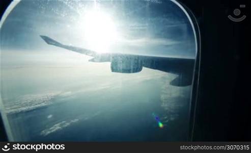 Scenic view from illuminator while traveling by air. Plane wing with sun flare and clouds beneath