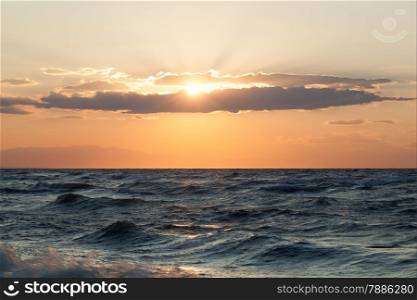 Scenic view of rough wavy sea and evening sun shining through the clouds