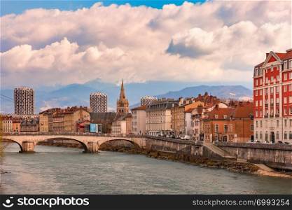 Scenic view of the banks of the Isere river and bridge, Collegiate Church of Saint-Andre with French Alps on the background, Grenoble, France. Church, Isere river and bridge in Grenoble, France