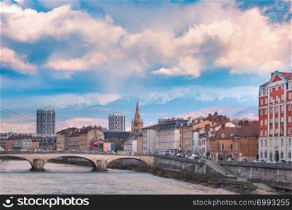 Scenic view of the banks of the Isere river and bridge, Collegiate Church of Saint-Andre with French Alps on the background, Grenoble, France. Church, Isere river and bridge in Grenoble, France