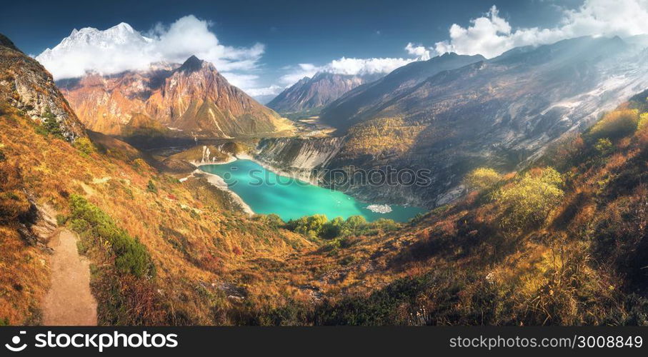 Scenic view on high Himalayan mountains, amazing mountain lake with turquoise water, hills, yellow grass, trees and blue sky with clouds at sunset in Nepal. Panoramic landscape with mountain valley