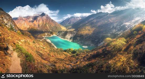 Scenic view on high Himalayan mountains, amazing mountain lake with turquoise water, hills, yellow grass, trees and blue sky with clouds at sunset in Nepal. Panoramic landscape with mountain valley