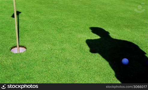 Schatten eines Golfspielers ist sichtbar, schlagt den Ball und erzielt einen Treffer, shadow of a golfer makes his hit, ball runs in hole