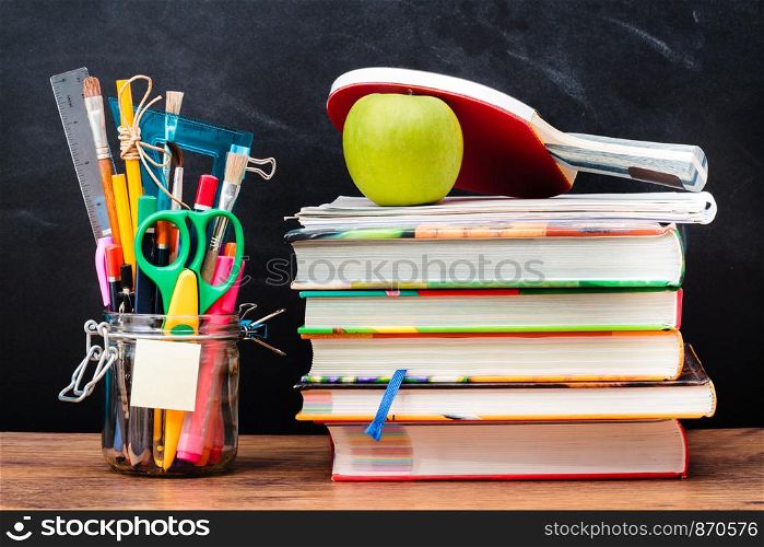 School accessories, books on a wooden desk with blackboard in the background