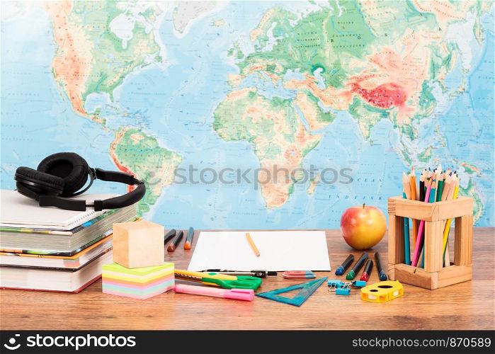 School accessories, books on a wooden desk with map of the world in the background. Front view