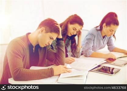 school and education concept - group of tired students with notebooks at school. students with notebooks and tablet pc at school