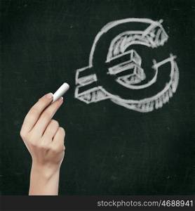 School blackboard and hand with chalk writing euro symbol on it