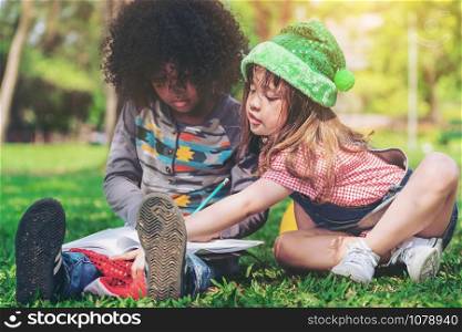 School boy and girl reading book together in the park. Education and friends concept.