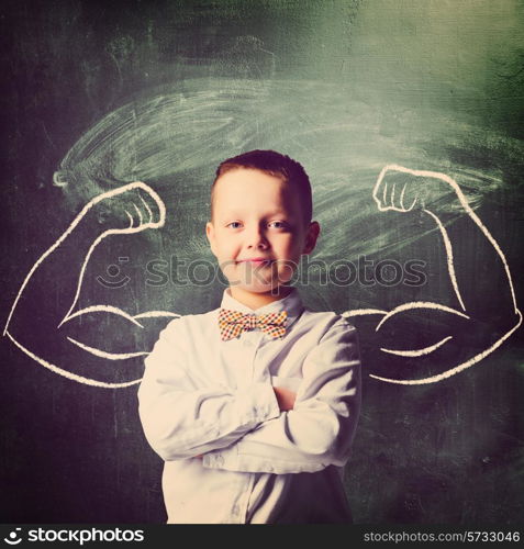 school boy is standing with strong hands on blackboard behind him