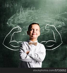 school boy is standing with strong hands on blackboard behind him