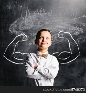 school boy is standing with strong hands on blackboard behind him. school boy