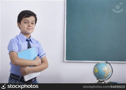 school boy standing infront of blackboard with a book