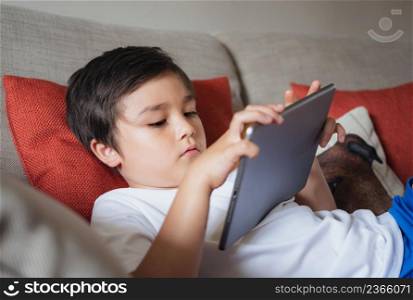 School boy using tablet studying online on internet, Kid playing game or watching cartoon on digital pad, Happy Child relaxing at home, Children with technology and social network concept