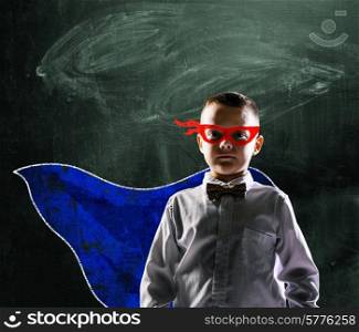 school boy wearing a superhero costume with blackboard behind him. superhero school boy