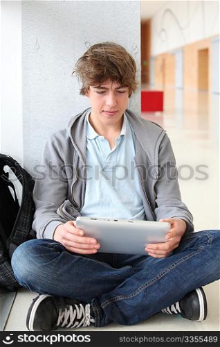 School boy with electronic tablet sitting in hall