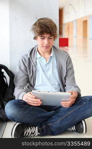 School boy with electronic tablet sitting in hall