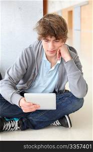 School boy with electronic tablet sitting in hall