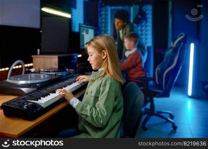 School children creating music at sound record studio, focus on girl playing synthesizer. School children at sound record studio