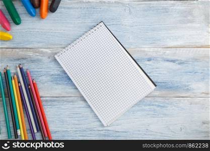 school children's concept. colored pencils, crayons and Notepad on blue and white scuffed vintage wooden background. the view from the top. Flat lay