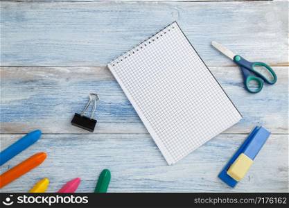 school children&rsquo;s concept. colored pencils or crayons,scissors,stapler and Notepad on blue and white scuffed vintage wooden background. the view from the top. Flat lay