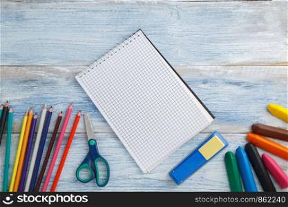 school children's concept. colored pencils or crayons,scissors,stapler and Notepad on blue and white scuffed vintage wooden background. the view from the top. Flat lay