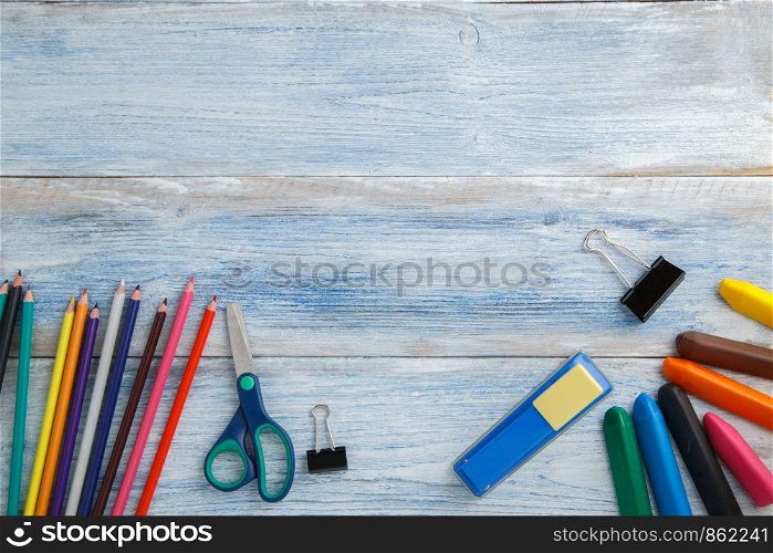 school children's concept. colored pencils or crayons,scissors,stapler on blue and white scuffed vintage wooden background. the view from the top. Flat lay