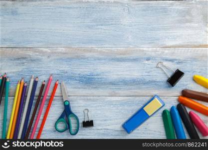 school children's concept. colored pencils or crayons,scissors,stapler on blue and white scuffed vintage wooden background. the view from the top. Flat lay