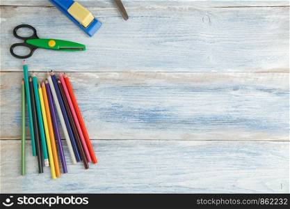 school children's concept. colored pencils,stapler and scissors on a blue and white scuffed vintage wooden background. the view from the top. Flat lay