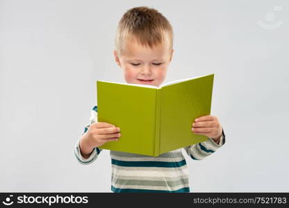 school, education and childhood concept - portrait of smiling little boy reading book over grey background. portrait of smiling boy reading book