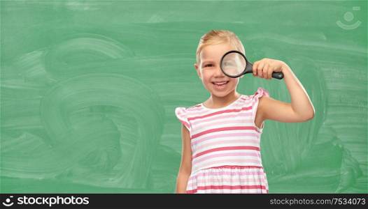 school, education and discovery concept - happy girl looking through magnifying glass over green chalkboard background. girl looking through magnifying glass at school