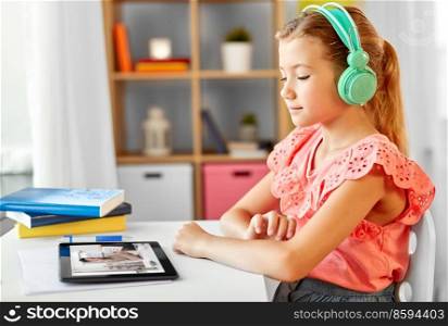school, education and distance learning concept - little student girl in headphones with tablet computer having online class at home from top. student girl in headphones learning online