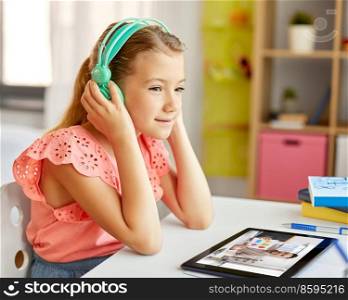 school, education and distance learning concept - little student girl in headphones with tablet computer having online class at home from top. student girl in headphones learning online