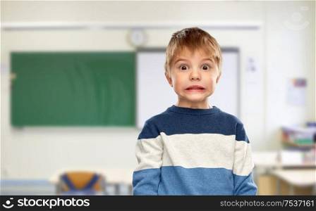 school, education and expressions concept - shocked little boy in striped pullover over classroom background. shocked little boy at school
